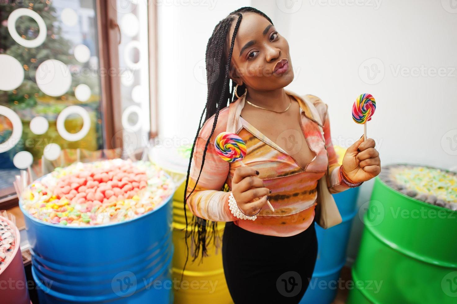 Afro-Amerikaanse duizendjarige dame bij snoepwinkel met lolipops. foto