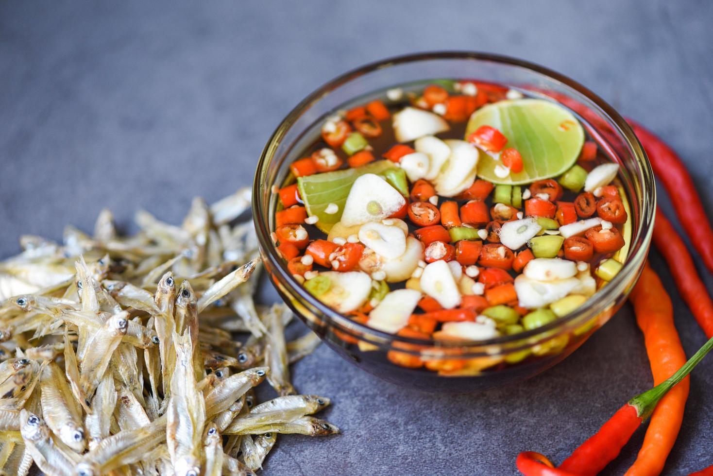 vissaus op glazen kom en verse chili knoflook citroen limoen en kleine gedroogde vis op zak, vissaus verkregen uit gefermenteerde vis of klein waterdier, gefermenteerd voedsel foto