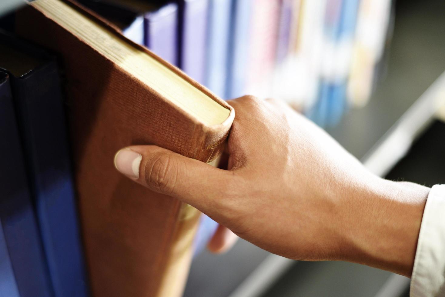 jonge mensenstudent die een boek bij de hand houdt of een boek op boekenplank in de bibliotheekboekenplankenachtergrond plukt - de studieconcept van het bedrijfsonderwijs foto