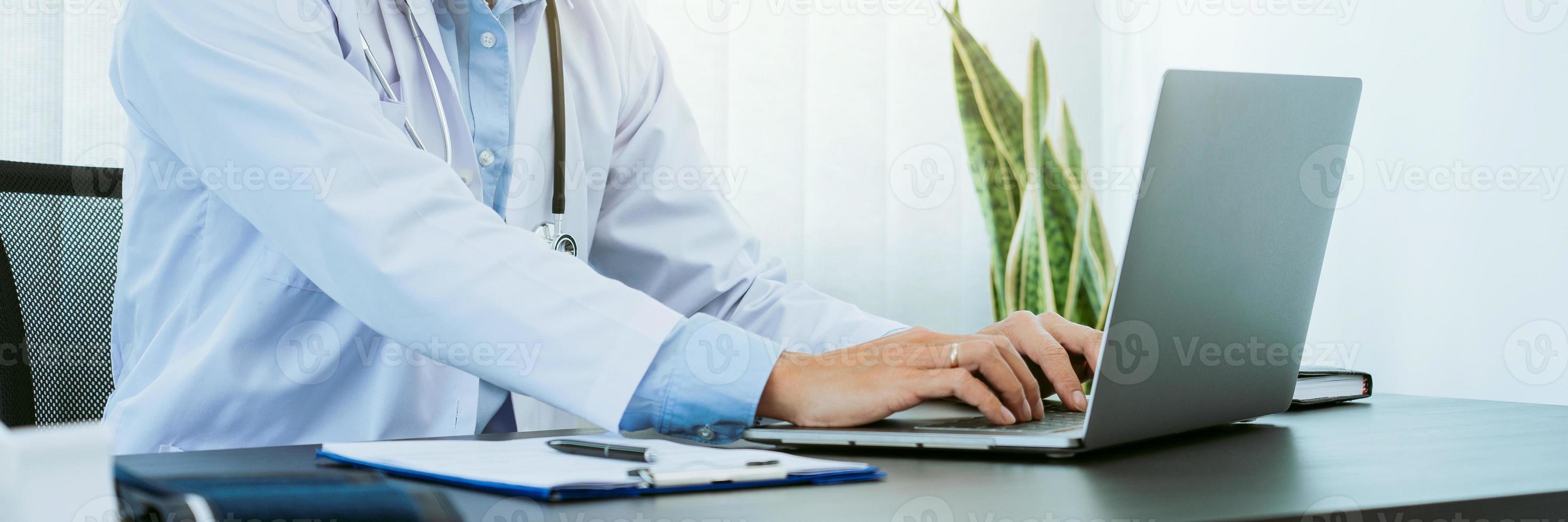 dokter zat op kantoor op een laptopcomputer te werken terwijl hij een masker droeg. foto