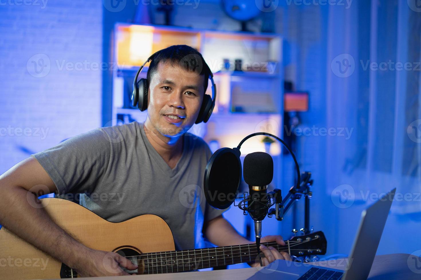 aziatische man youtuber live streaming performance gitaar spelen en een lied zingen. aziatische man die gitaar lesgeeft en online zingt. muzikant die muziek opneemt met laptop en akoestische gitaar speelt. foto