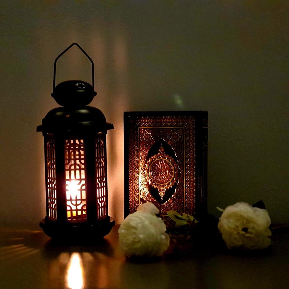 de lantaarn van ramadan is zwart van kleur, lichtgevend, versierd met houten motieven, naast de heilige koran, met een paar witte rozen foto