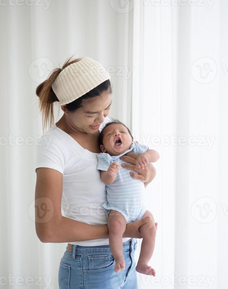 gelukkige aziatische moeder die een mooie pasgeboren baby vasthoudt in de kinderkamer, moeder die haar pasgeboren baby knuffelt en bij het raam staat foto