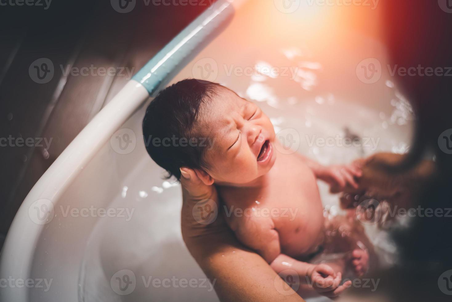 aziatisch babymeisje huilend in bad door moeder thuis, aziatische babydouche voor kinderen. baby familie concept. foto