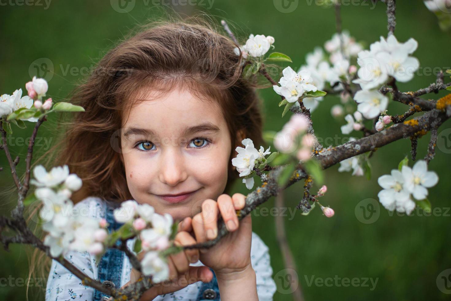 een schattig klein meisje van 5 jaar oud in een bloeiende witte appelboomgaard in het voorjaar. lente, boomgaard, bloei, allergie, lentegeur, tederheid, zorg voor de natuur. portret foto