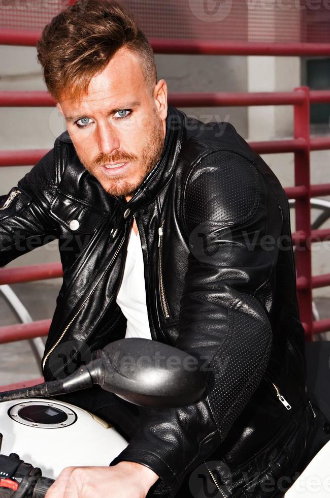 trendy jonge man met zwarte leren jas op een motorfiets met een uitdagende look. verticaal beeld. foto