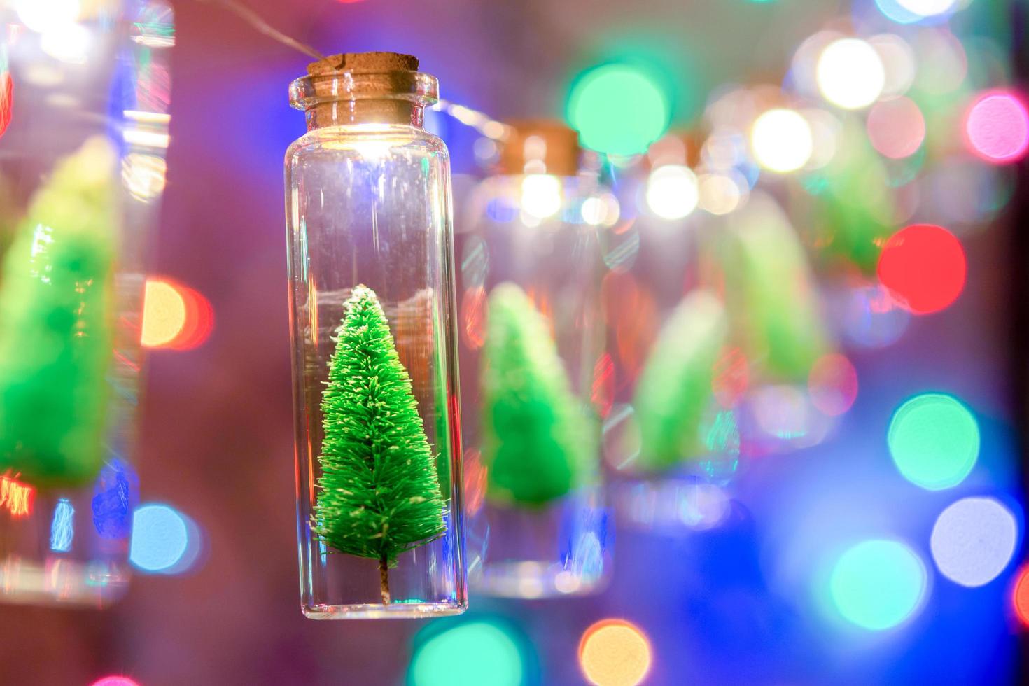 vrolijk kerstfeest en een gelukkig nieuwjaar. hangende kleine kerstboom in glazen pot op pijnboomtakken kerstboomslinger en ornamenten over abstracte bokeh foto