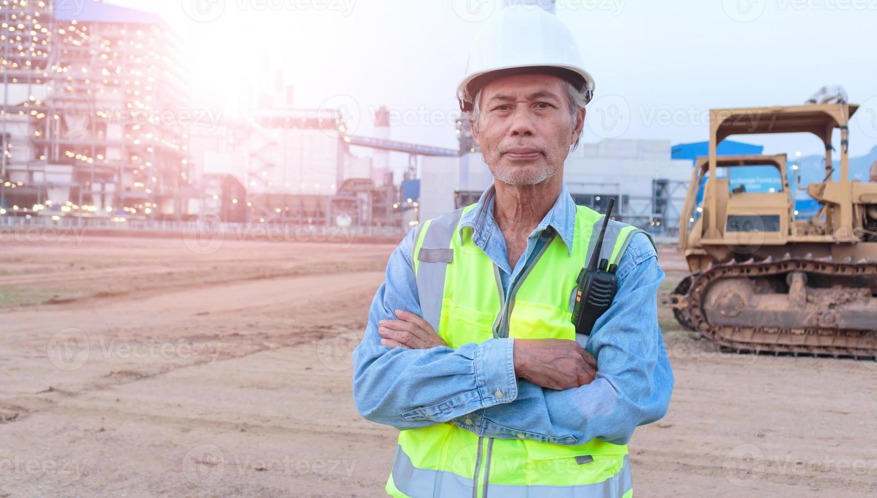 Aziatische senior mannelijke ingenieur met veiligheidsvest en helm inspecteert civiele werken de hoofdbouwingenieur gebruikt een walkietalkie om de graafmachine te beheren. foto