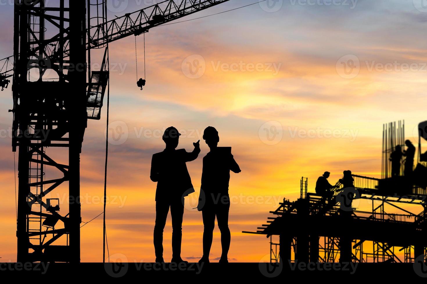 silhouet van ingenieur en werknemer op bouwplaats, bouwplaats bij zonsondergang in de avondtijd foto