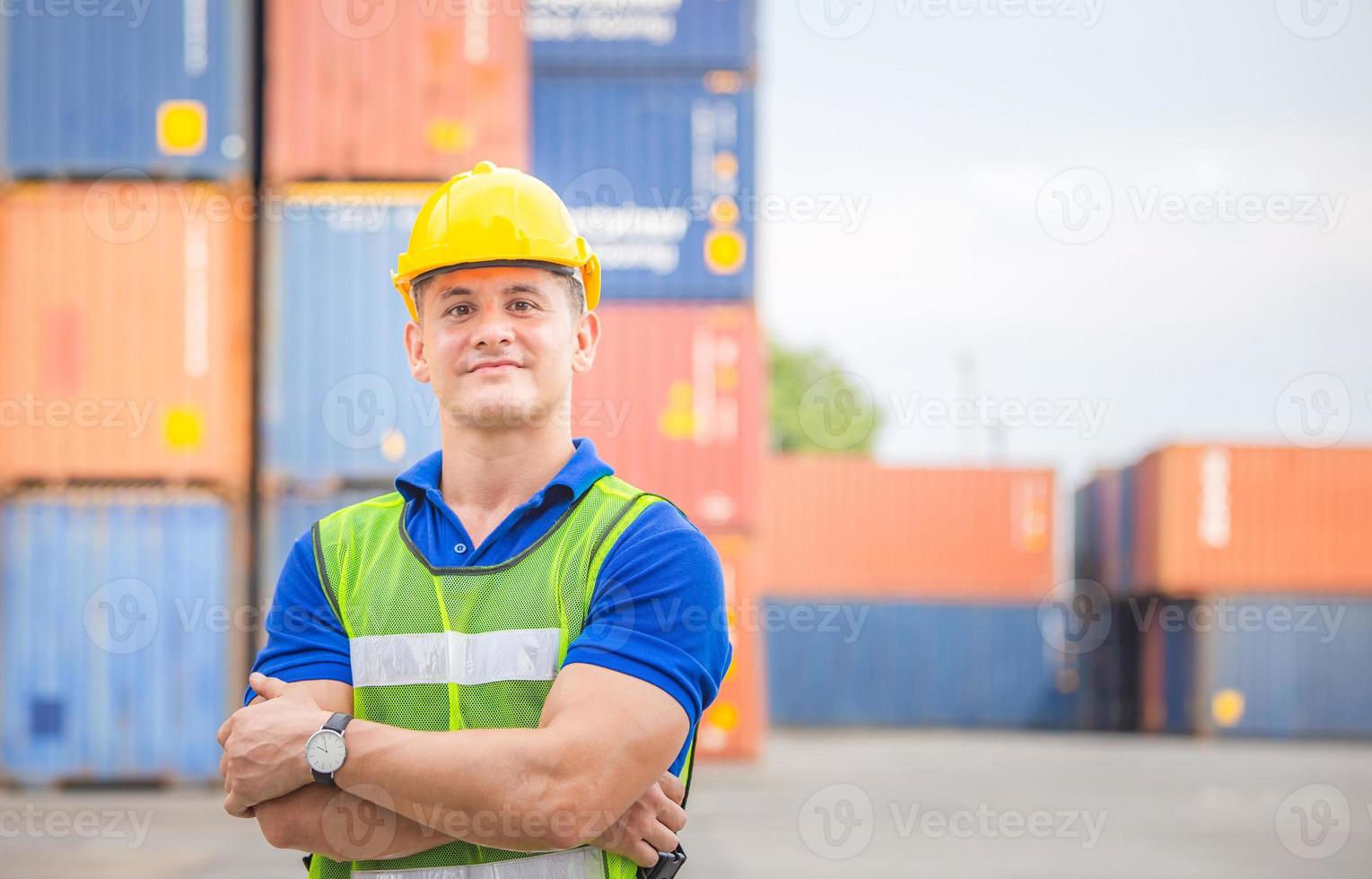 vrolijke fabrieksarbeider man in harde hoed glimlachend en armen gekruist als teken van succes met wazig container vak achtergrond foto