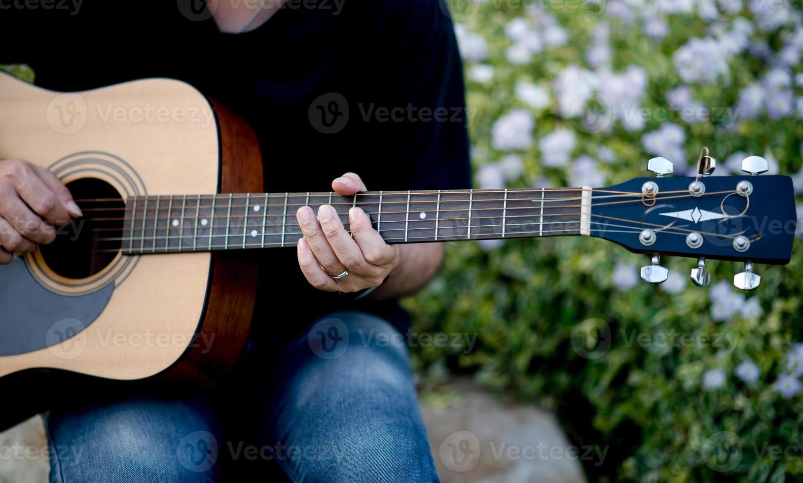 foto van een gitarist, een jonge man die gitaar speelt terwijl hij in een natuurlijke tuin zit, muziekconcept