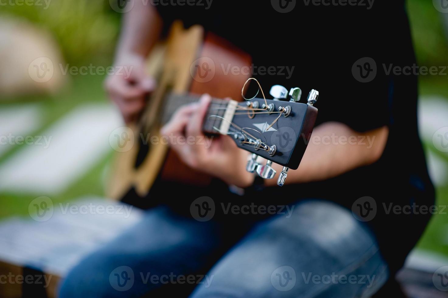 foto van een gitarist, een jonge man die gitaar speelt terwijl hij in een natuurlijke tuin zit, muziekconcept