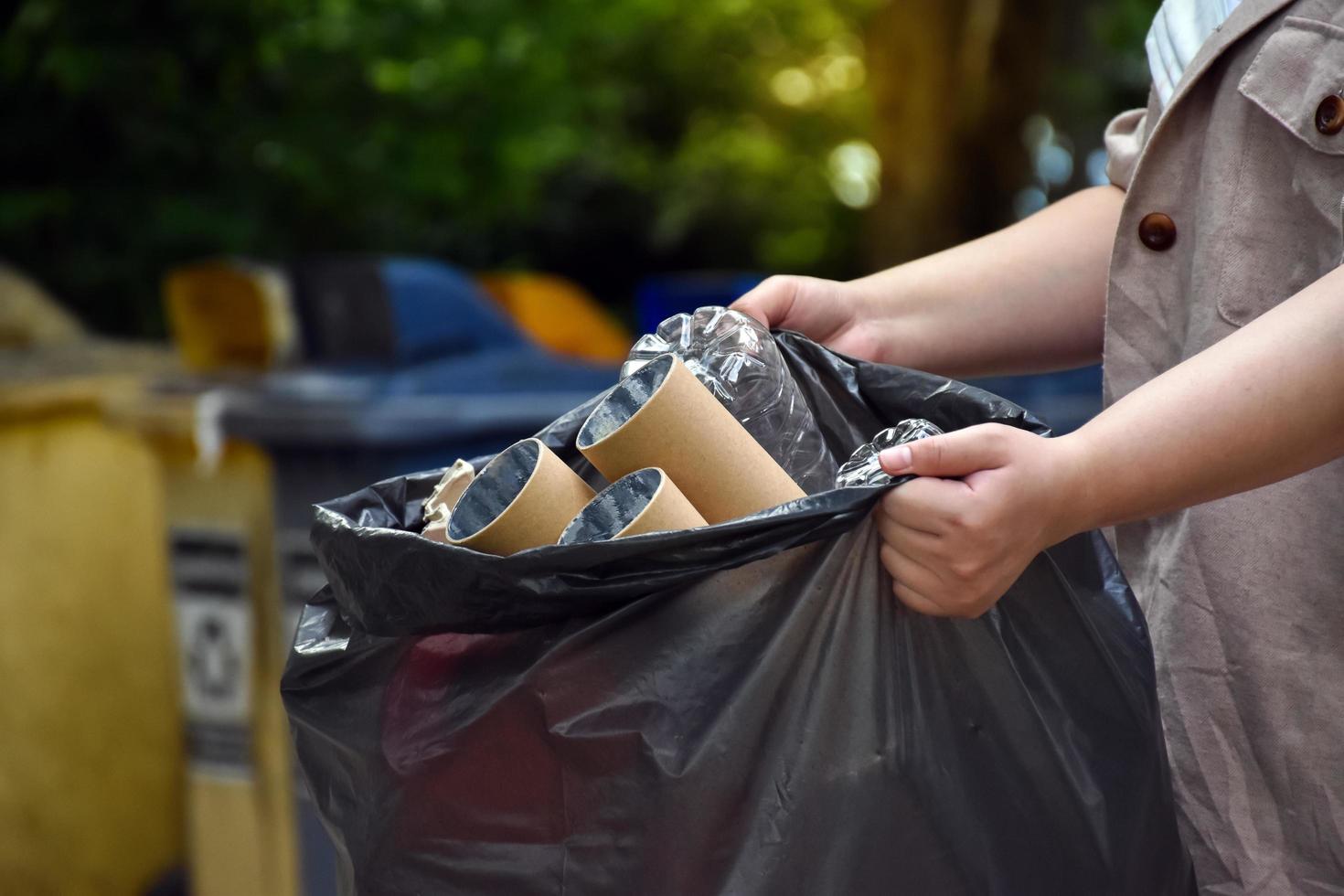 huiseigenaar draagt zwarte plastic zak die vol zit met afval, plastic flessen, dozen, melkflessen en gebruikt papier om afval thuis te scheiden en te beheren. zachte en selectieve focus op afval. foto