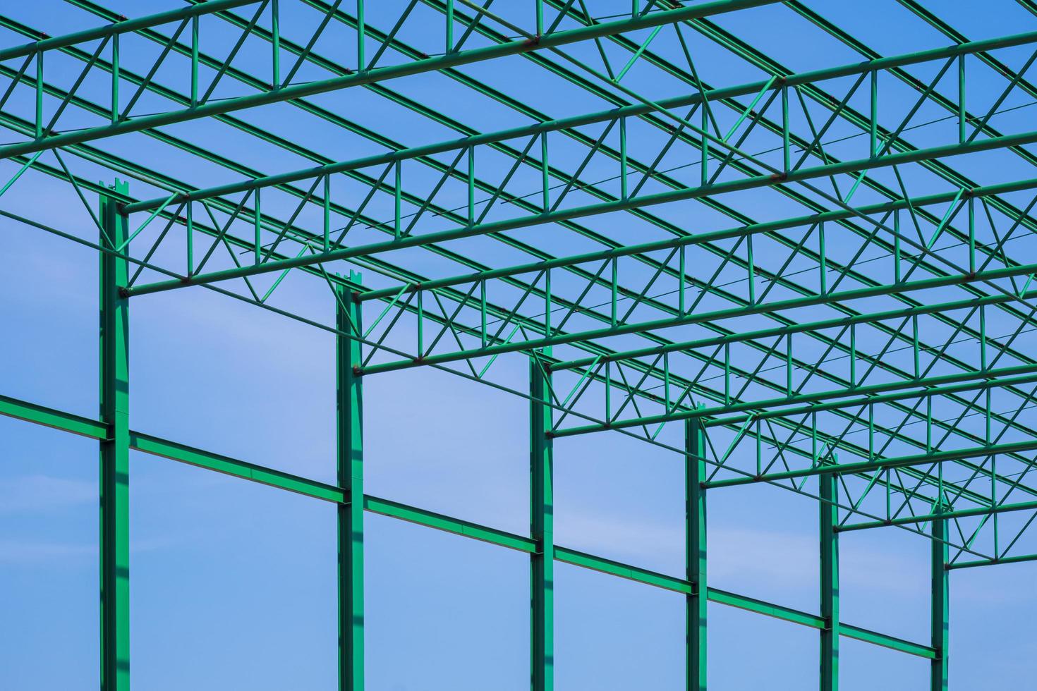 lage hoekmening van groen stalen dak van magazijnbouwstructuur in bouwgebied tegen blauwe hemelachtergrond foto