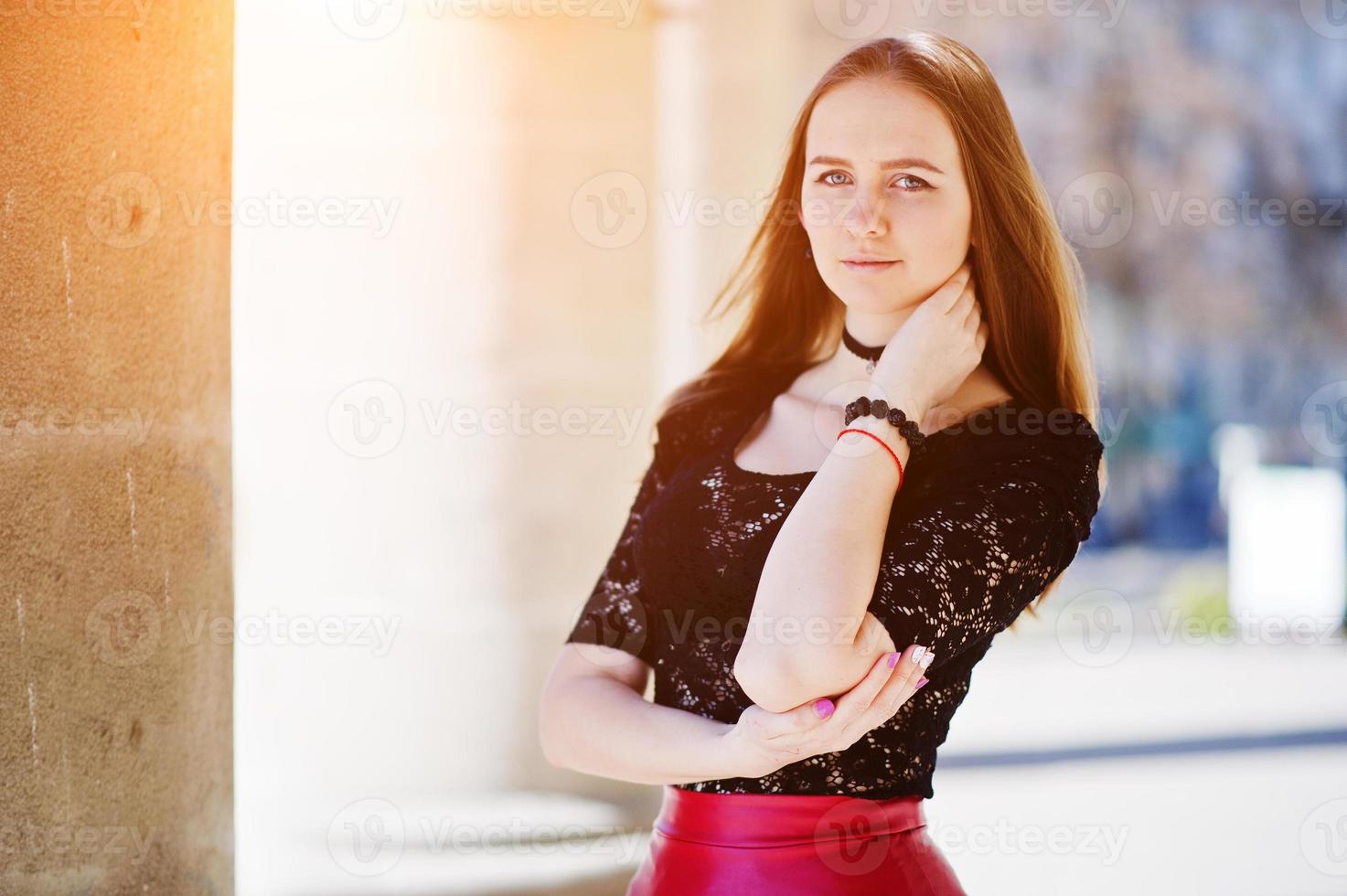 portret van meisje met zwarte choker ketting op haar nek en rode leren rok tegen stenen zuilen. foto