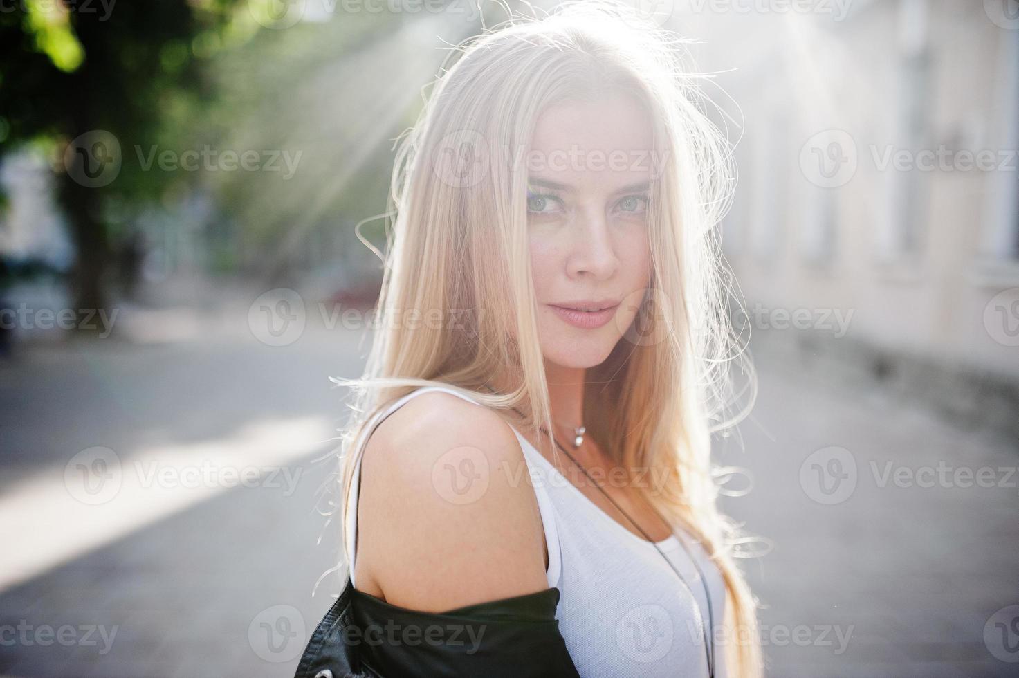 stijlvolle blonde vrouw draagt jeans, zonnebrillen en jas op straat op de zon. mode stedelijk model portret. foto