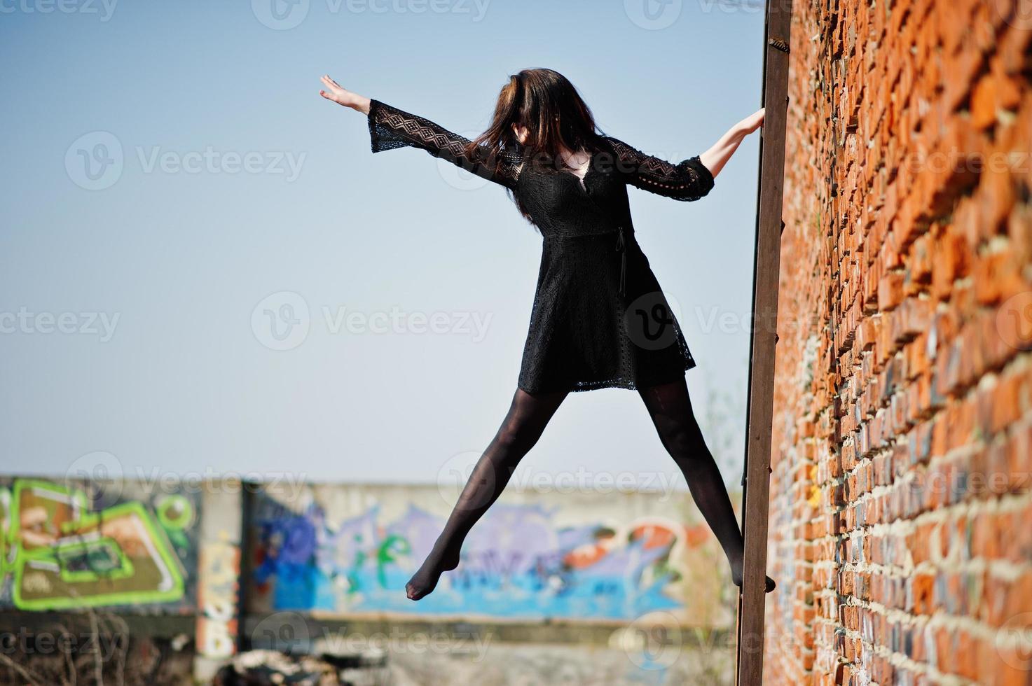 portret brunette meisje met rode lippen, gekleed in een zwarte jurk gesteld op het dak bij ladder. straatmodel. foto