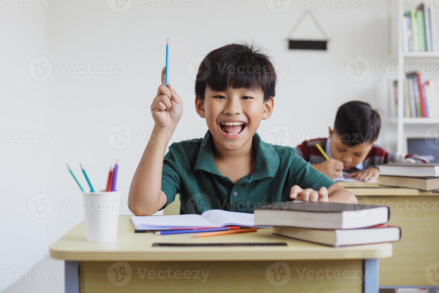 slimme en gelukkige Aziatische basisschooljongen die in de klas studeert foto