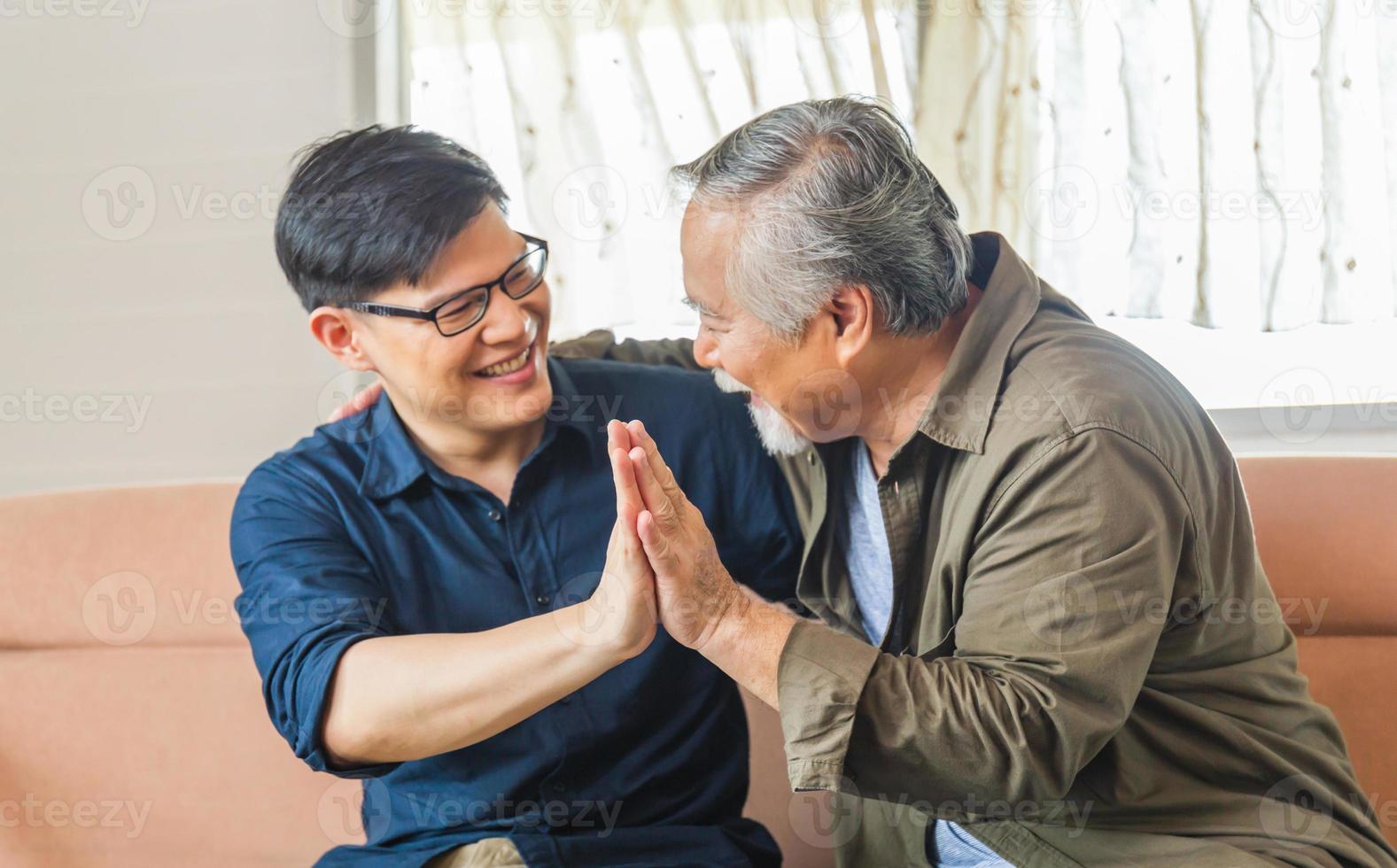 vrolijke senior Aziatische vader en zoon van middelbare leeftijd in de woonkamer, geluk Aziatische familieconcepten foto