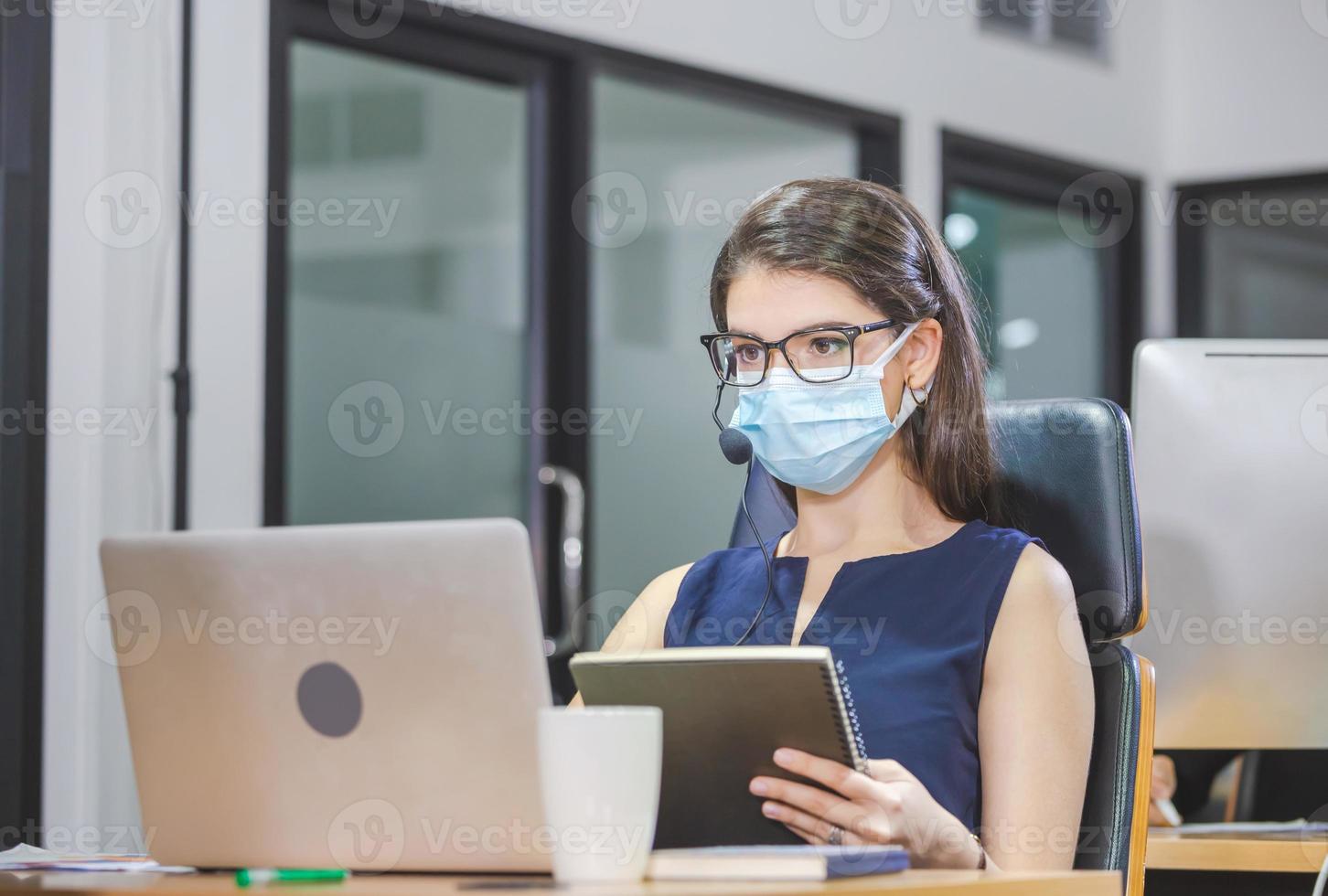 jonge vrouw telefoniste met headset draagt een beschermend gezichtsmasker tegen coronavirus, uitvoerend team van de klantenservice werkt op kantoor foto