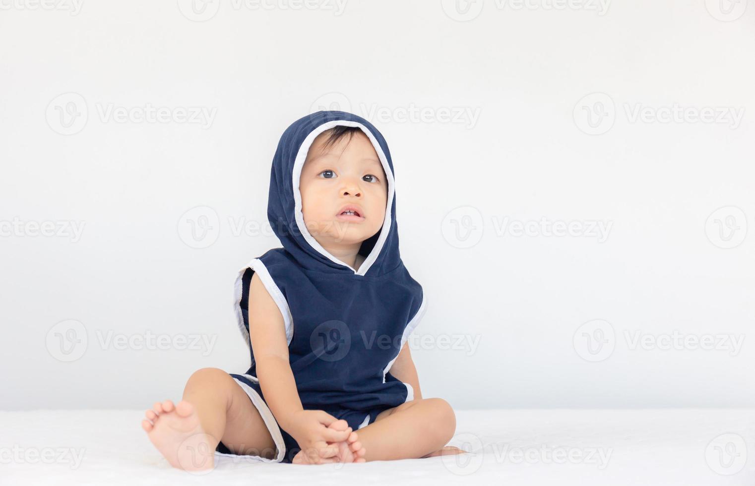 gelukkige babyjongen met blauwe capuchon zittend op bed, kinderen spelen concept foto