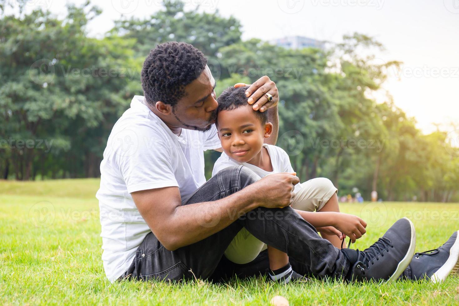 gelukkige afro-amerikaanse vader terwijl hij zijn zoon knuffelt en draagt, vader kuste zijn zoon in het park, vrolijk zwart familieconcept. foto