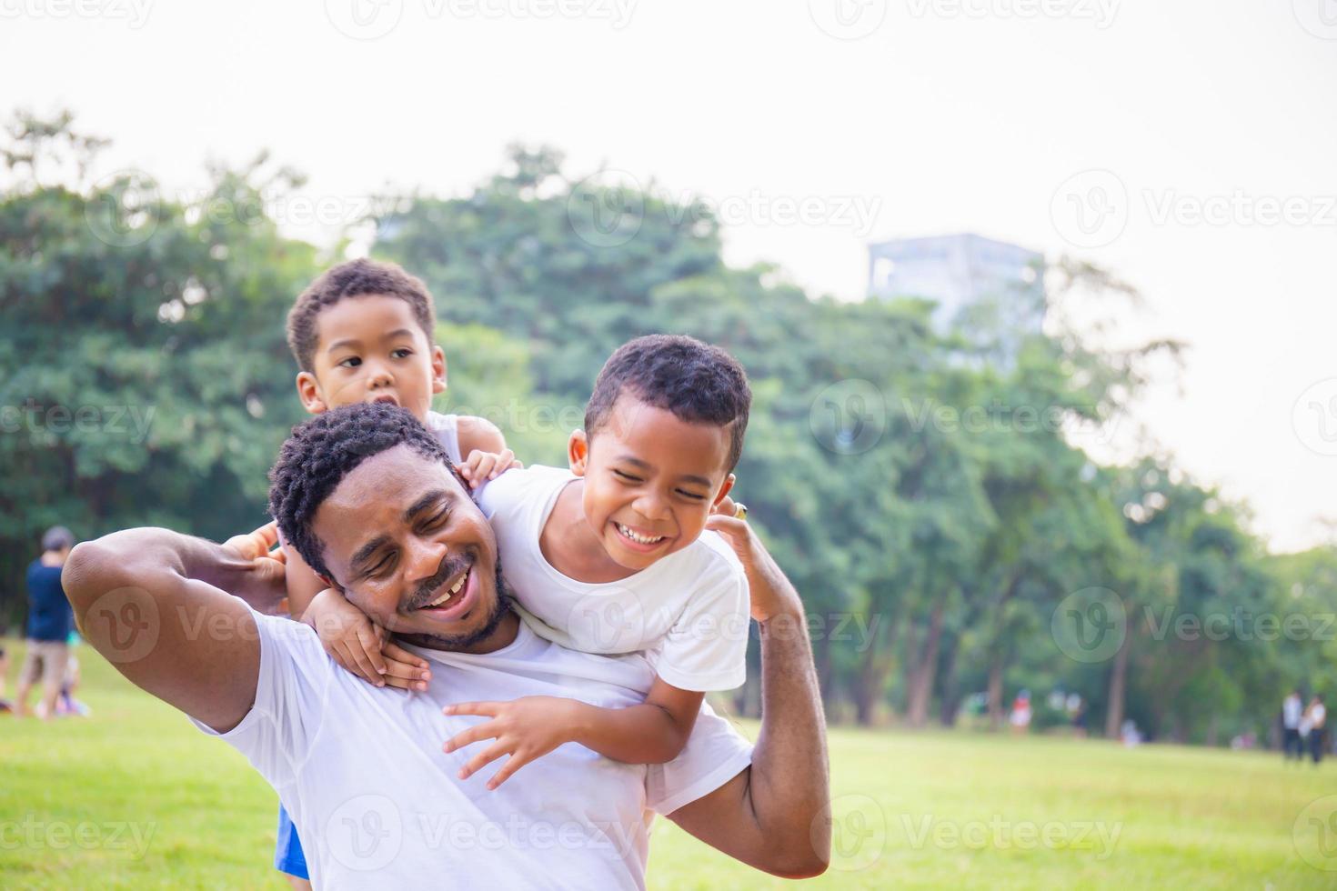 vrolijke afro-amerikaanse vader en twee zonen die in het park spelen, geluksfamilieconcepten, ouder en kind spelen in het park foto