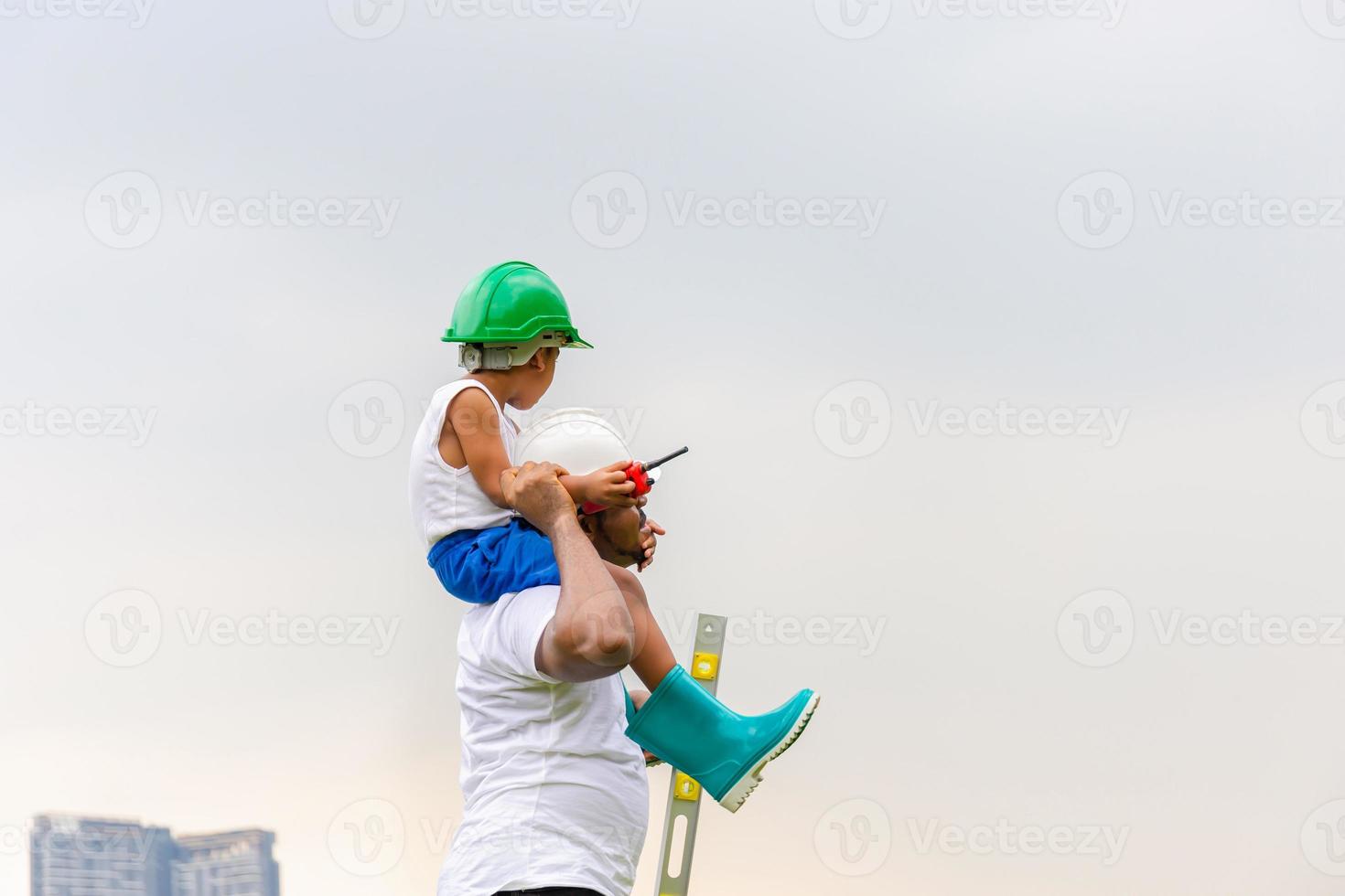 vrolijke Afro-Amerikaanse vader en zoon in harde hoed, gelukkige vader die zoon op schouders draagt foto