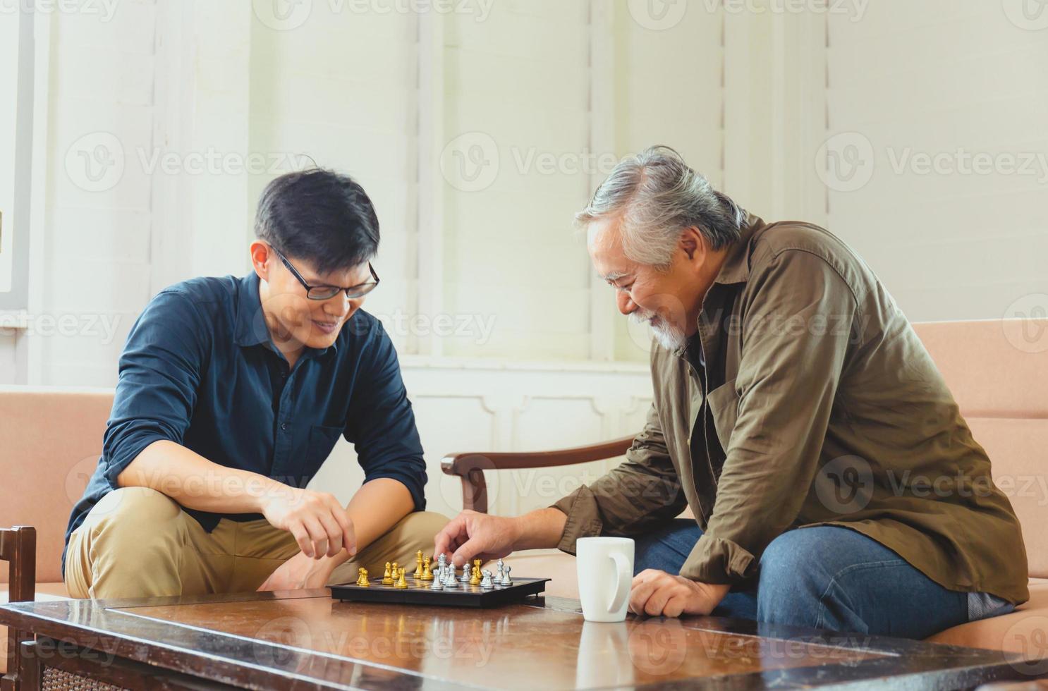 senior aziatische vader en zoon van middelbare leeftijd die schaakspel spelen in de woonkamer, geluk aziatische familieconcepten foto