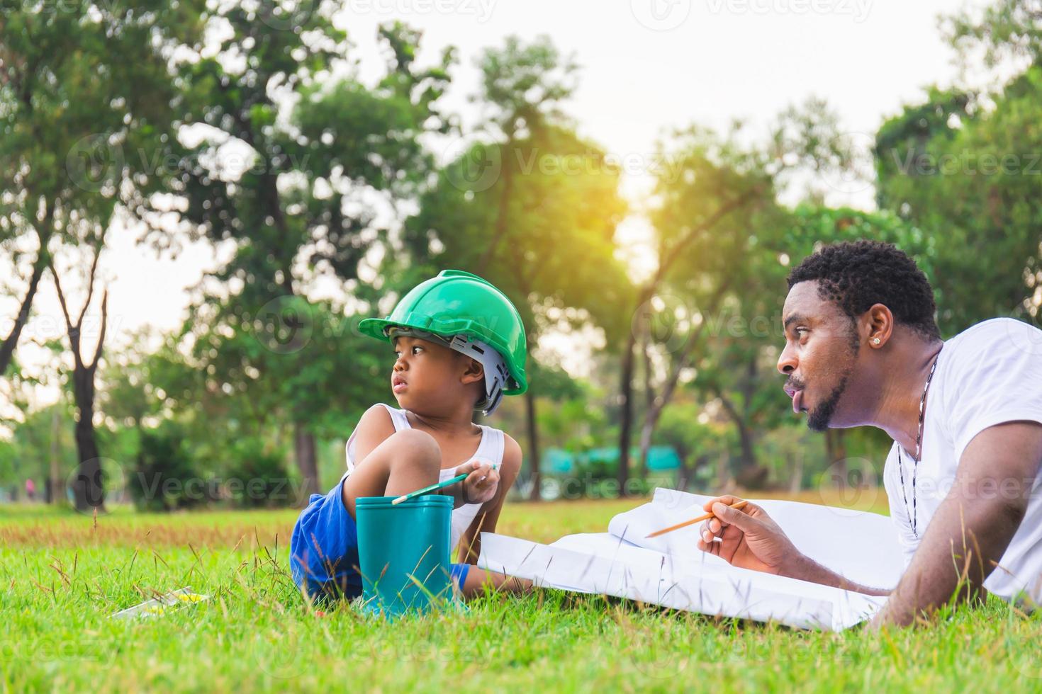 vrolijke Afro-Amerikaanse vader en zoon spelen in het park, ouder en kind tekenen en schilderen in het park, geluk familieconcepten foto