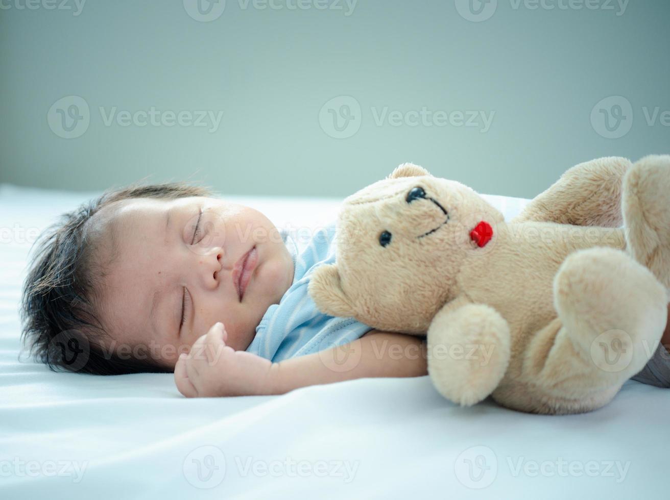 pasgeboren baby slaapt met haar teddybeer op het bed, nieuw gezin en liefdesconcept foto