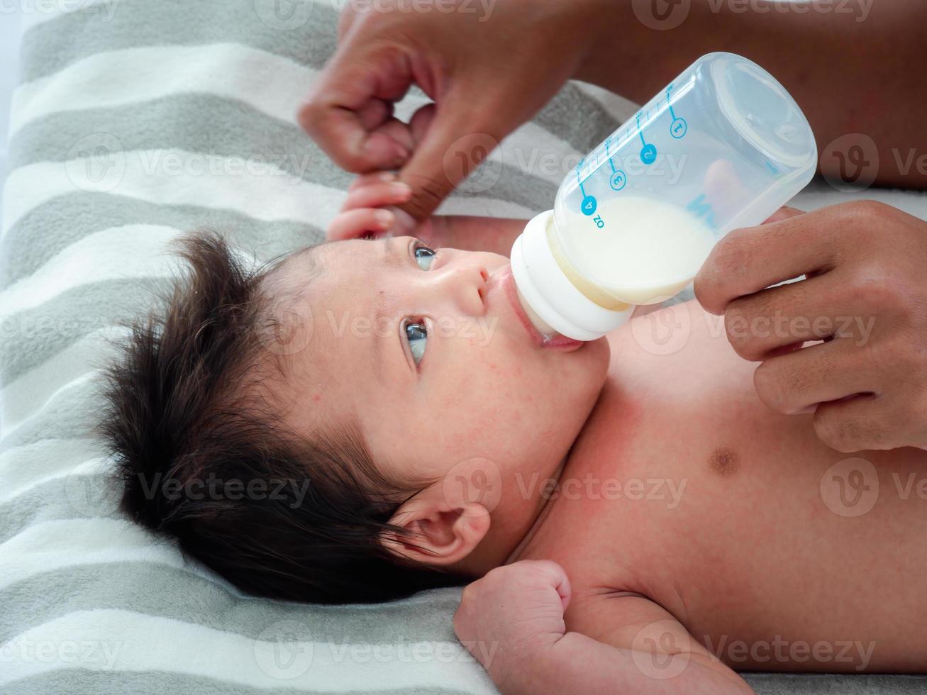 portret van aziatische moeder voedt de australische aziatische drie weken pasgeboren met melkformule uit een fles, concept van moederschap en kindertijd of baby liggend op het witte bed. foto