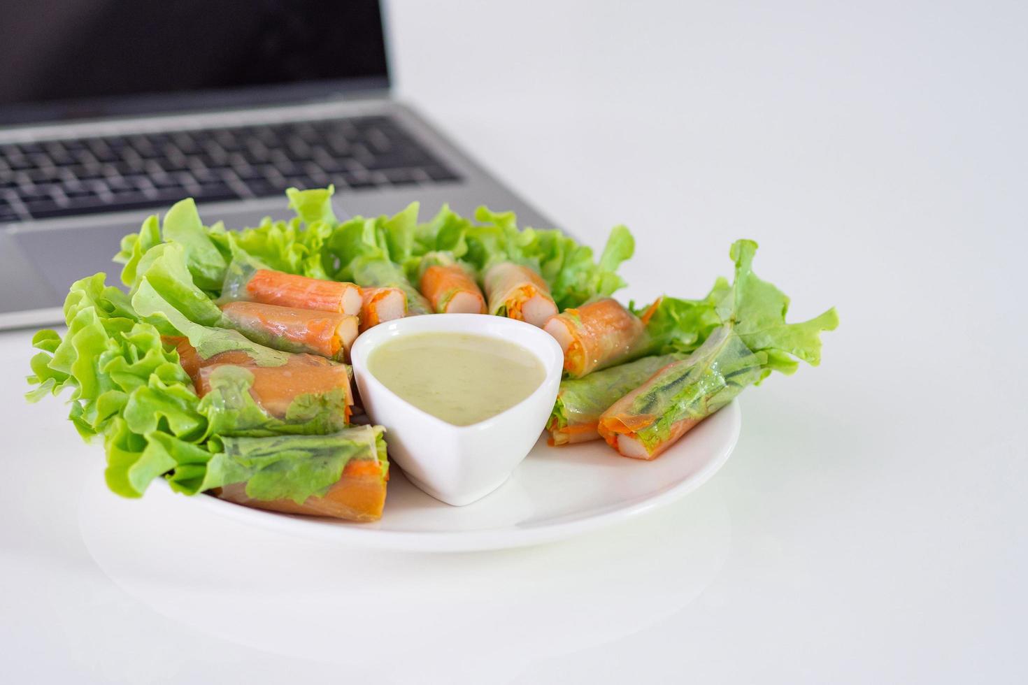 krabstick en groentensalade in noedelbuis op witte schotel bij laptop foto