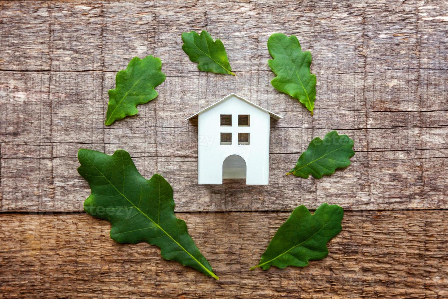 speelgoedhuis en groene eikenbladeren op houten achtergrond foto