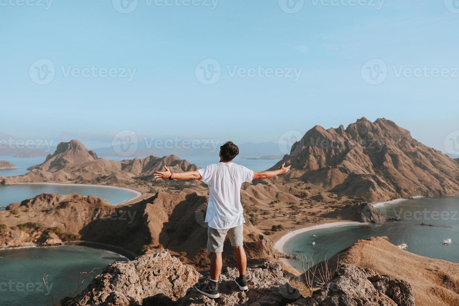 gelukkige man toerist die op de top van de rotsberg staat terwijl hij geniet van het uitzicht op zee foto