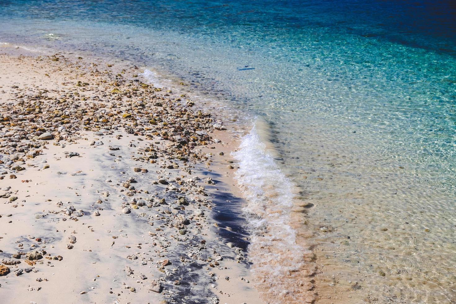 transparante zeekust en zachte golf met schuim op koraalzandige kustachtergrond foto