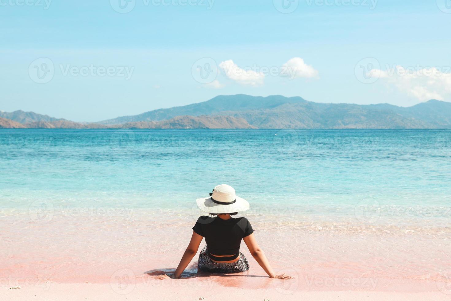 vrouw met zomerhoed die van de zomervakantie geniet en op het roze zandstrand van labuan bajo . zit foto