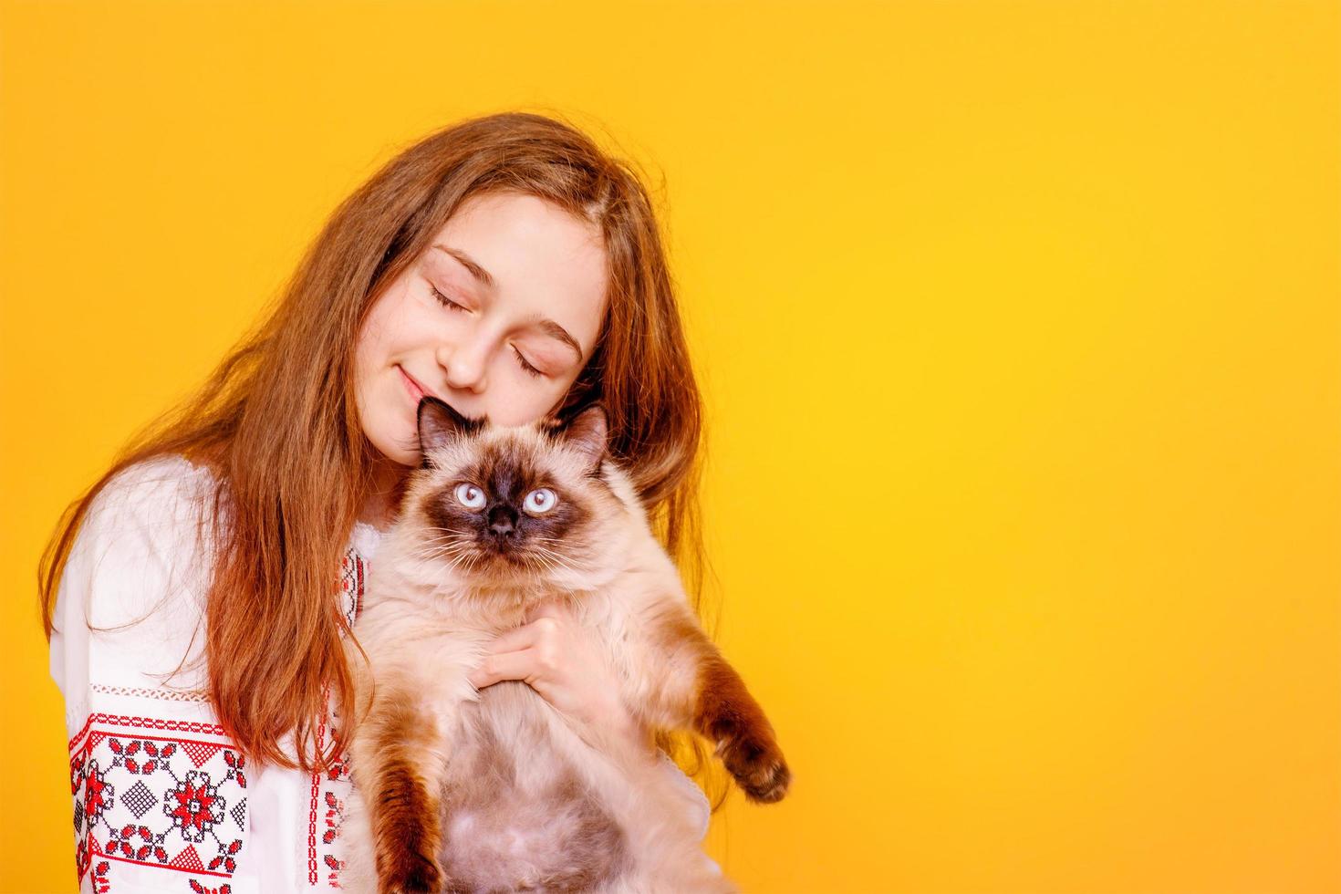 tienermeisje met een kat in haar armen. meisje op een gele achtergrond. het kind in een geborduurd overhemd. foto