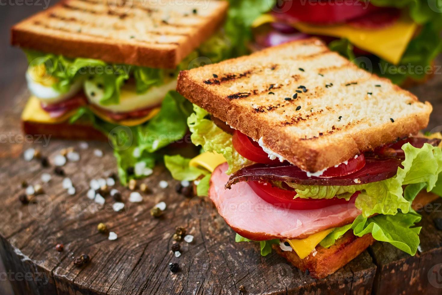 zelfgemaakte sandwich met ham, sla, kaas en tomaat op een houten ondergrond foto