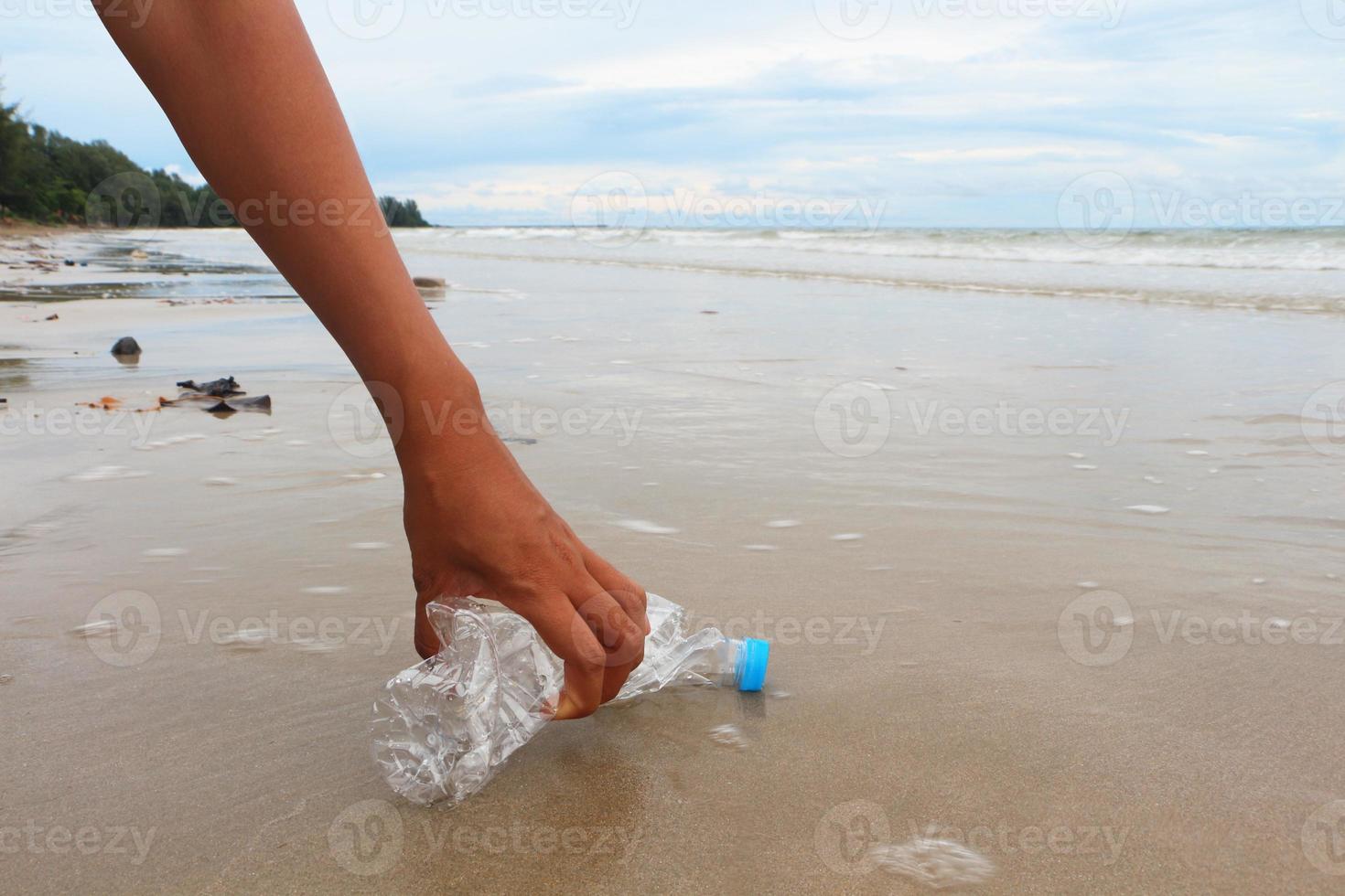 hand van vrouw plukt een lege plastic fles op het strand. foto