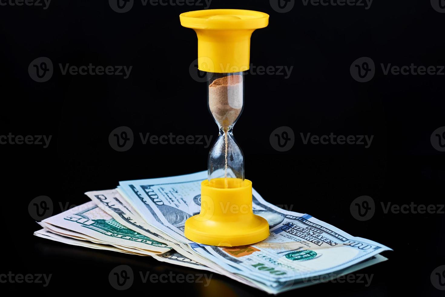 tijd is geld of tijdinvestering en pensioenbesparingsconcept. gele zandloper op stapel dollarbiljetten op een donkere achtergrond foto