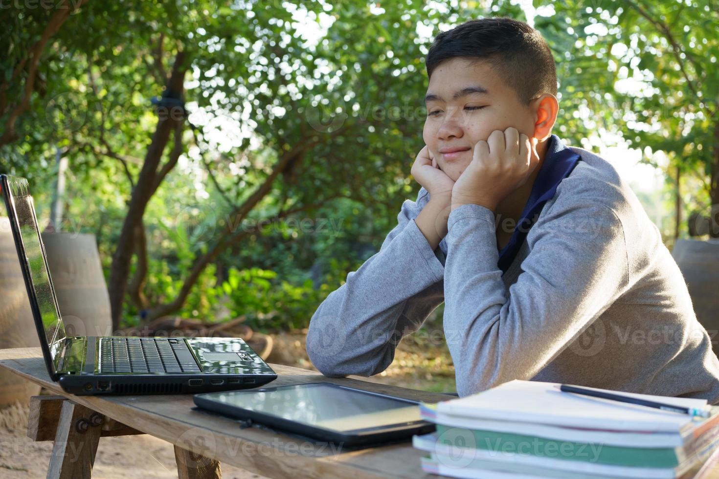 de jongen laat zijn kin op zijn handen rusten en studeert aandachtig en vrolijk online in een landhuis. foto
