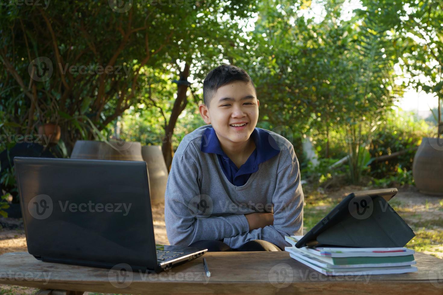 jongen kijken camera online studeren op een houten tafel met laptopcomputer en tablet in de ochtend in een landelijk huis. concept online onderwijs platteland en thuiswerken foto
