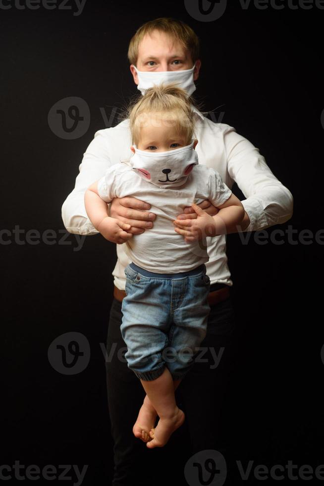 vader met een medisch masker houdt zijn dochtertje vast. het concept om kinderen te beschermen tijdens de epidemie van coronavirus foto