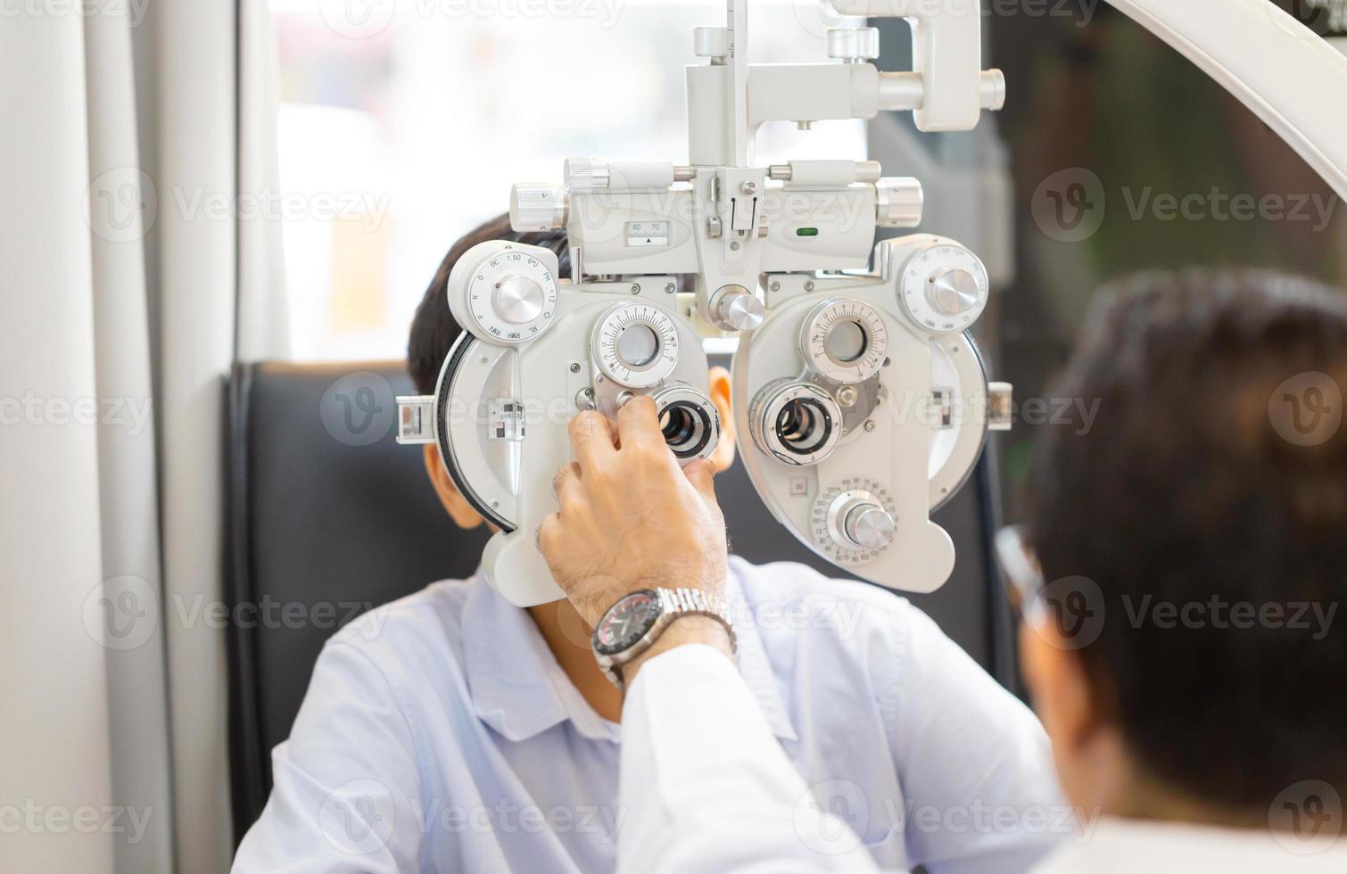 optometrist doet zichttest voor kindpatiënt in kliniek, jongen doet oogtest controleert onderzoek met optometrist in optische winkel foto
