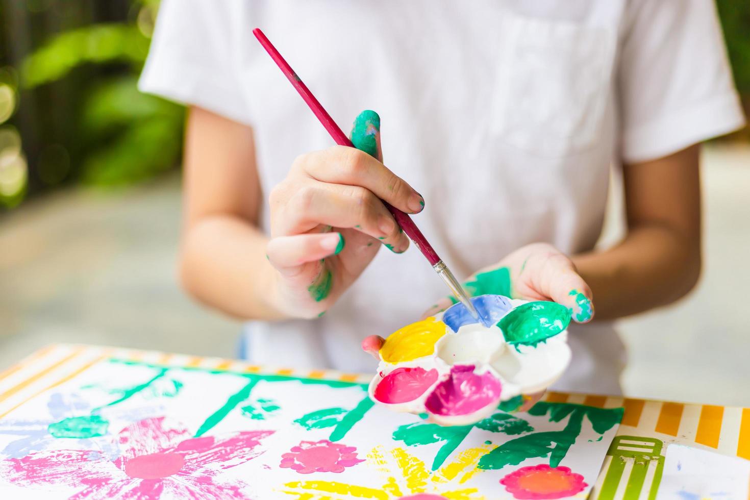 kind aan tafel tekent met waterverf, vrolijk klein schattig meisje dat speelt en leert met het inkleuren van de kleuren foto