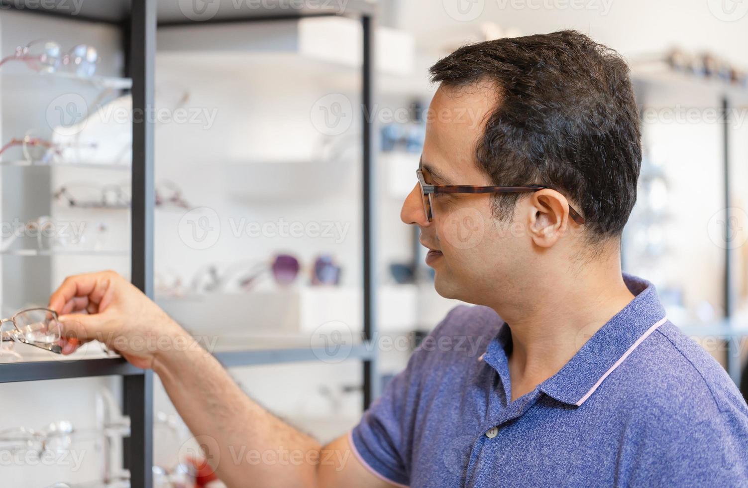 portret van indiase man die een bril kiest in een optiekwinkel, een knappe man met een bril in een optische winkel, een jonge man die een bril probeert foto