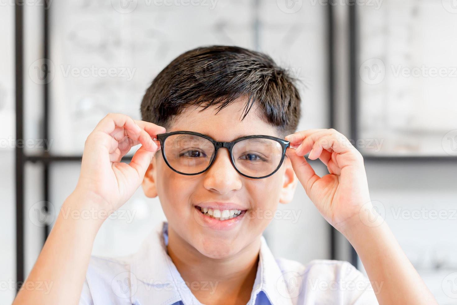 lachende indisch-thaise jongen die een bril kiest in de optiekwinkel, portret van een kind met een gemengd ras etniciteit dat een bril draagt in de optische winkel foto