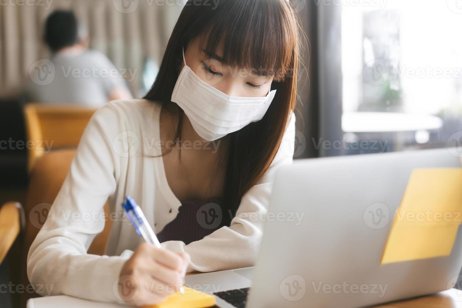 jonge volwassen aziatische student vrouw met gezichtsmasker voor virus corona of covid 19 studie in café. foto