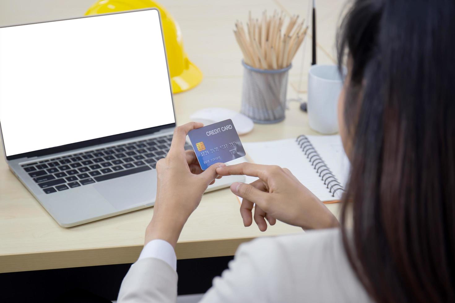 een jonge professionele Aziatische zakenvrouw die een laptop en een creditcard gebruikt om online te betalen terwijl ze aan haar bureau zit. foto